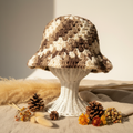 Handmade crochet bucket hat in brown tan and cream variegated yarn on wicker stand with pampas grass