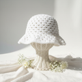 Handmade white crochet bucket hat with open lace pattern on wicker stand with white flowers